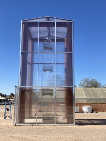 A multi-story solar tower contains suspended, large drying baskets. The tower is enclosed in a clear, plexi-glass like material.